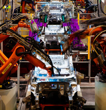 Automated robotic arms are welding at an automobile production plant.