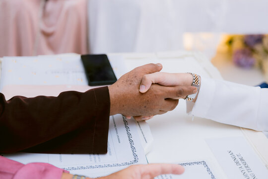 A meaningful close-up of the traditional handshake (Akad Nikah) between the groom and the marriage officiant during an Islamic solemnization ceremony.
