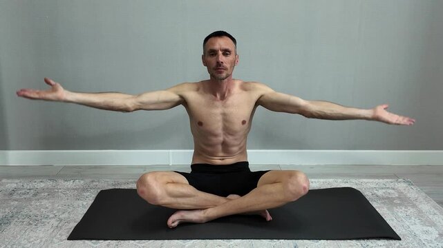 Athletic man with a muscular body meditating in a lotus position on a yoga mat. Serene male practicing breathing exercises for mindfulness