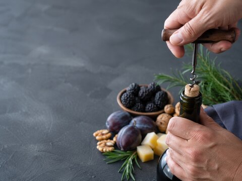 Abrir una botella de vino con una sacacorchos y una charola de frutas y nueces en la mesa