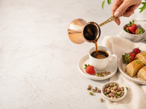 Preparar caf&eacute; en una taza blanca con pistachos y dulces en un plato al lado