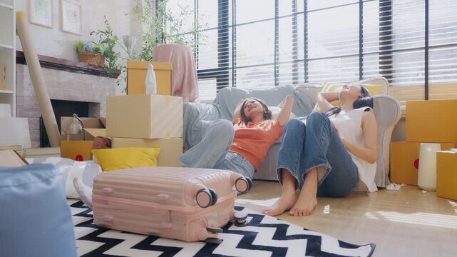 Happy two Asian women friend picking up things out to a paper box while preparing to move in of the new home. Relocation concept