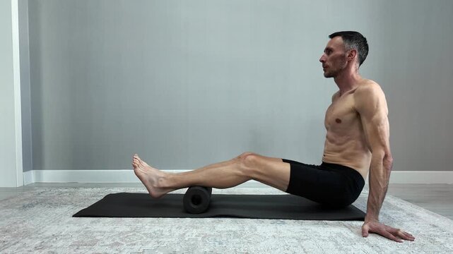 Athletic man massaging his hamstrings and calf muscles on a foam roller. Self-myofascial release for workout recovery at home