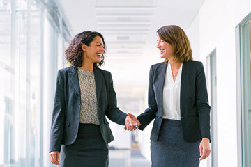 Fototapeta premium Diverse Businesswomen Holding Hands in Office Corridor, Smiling and Communicating