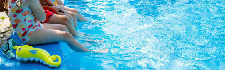 Obraz premium Happy children sitting by swimming pool and splashing water with legs