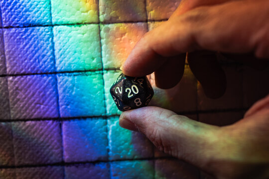 Macro Close Up of a Hand Holding a D20 Polyhedral Dice Over a Vibrant Rainbow Colored Fantasy Table