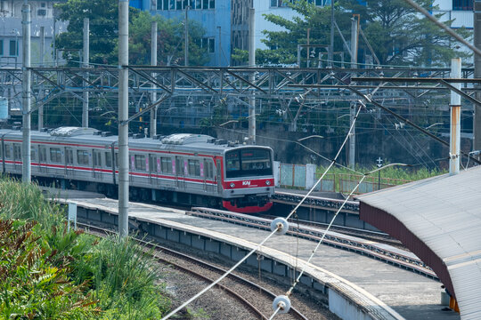 Jakarta, Indonesia - July 02, 2026: KAI Commuter train traveling on curved tracks at Kampung Bandan Station with green trees and overhead catenary lines.