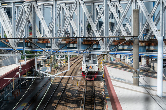 Jakarta, Indonesia - July 02, 2026: KAI locomotive passing beneath steel truss bridges and overhead catenary lines at Kampung Bandan Station.