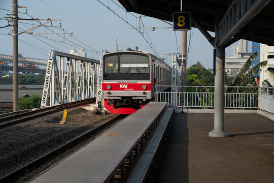 Jakarta, Indonesia - July 02, 2026: A KAI Commuter train crosses a steel truss bridge near Kampung Bandan Station beneath overhead catenary wires.