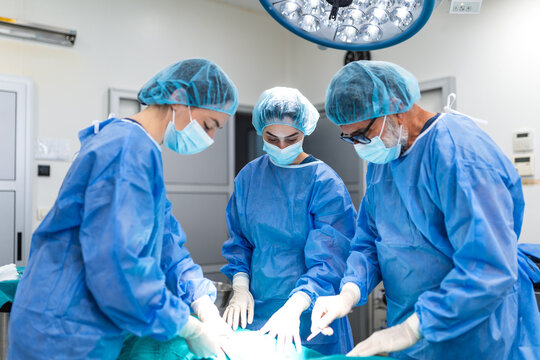 Team of surgeons and nurses performing complex operation in hospital. Medical professionals wearing scrubs and protective gear working in modern operating theater. 