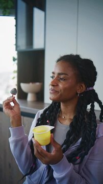 Woman enjoys a snack of yellow pudding while sitting in a modern kitchen during the daytime in a casual and relaxed setting