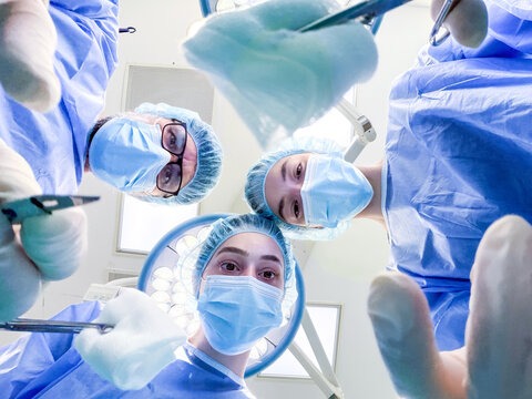 Doctors performing operation, view from patient perspective. Medical team looking down with surgical tools in operating room. Healthcare, surgery, procedure and intensive care medical concept.