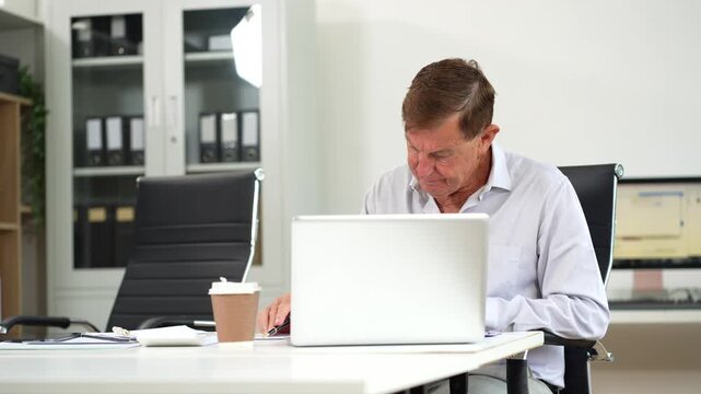 Mature businessman calculate and analyzing graph document financial with report and laptop in office.