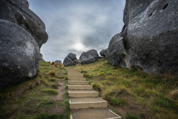 A wooden staircase descends through massive limestone boulders at Castle Hill (Kura Tawhiti), framed by two towering weathered rock formations on either side Canterbury New Zealand © ting_149