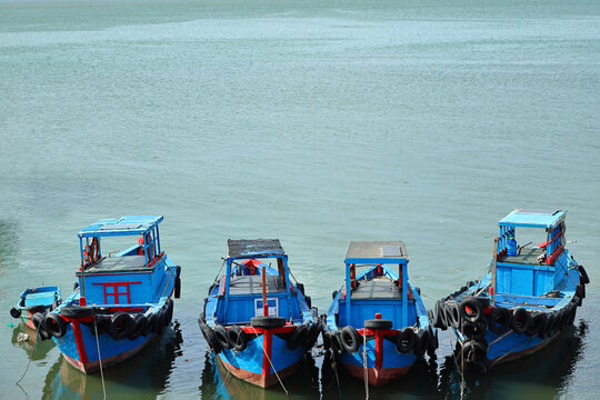 High-angle shot of four traditional wooden blue fishing boats parked in a row on calm sea water with extensive copy space. Excellent for tourism marketing, maritime travel blogging, and commercial fis