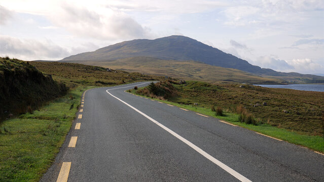 Curving Connemara road beside Lough Inagh in Galway Ireland with peaceful water, dramatic mountain backdrop and rural scenic landscape