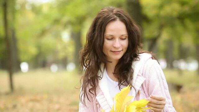 A happy young family with a child is having fun in the autumn park. Mother and daughter is hugging outdoors against blurred autumn leaves background. Slow motion