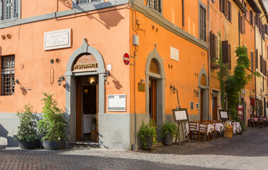 Obraz premium View of cobbled street with colorful old houses and cafe tables on a sunny morning in Trastevere, Rome, Italy.