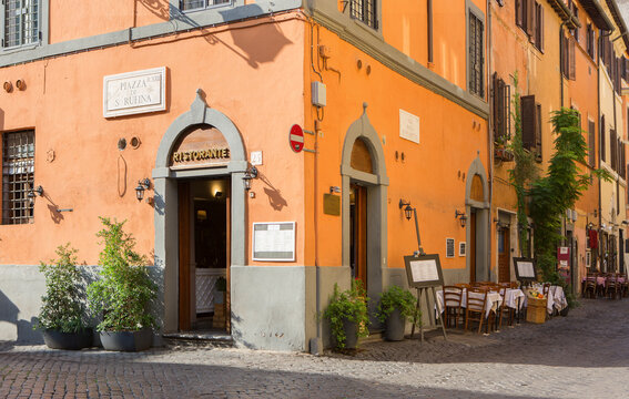 View of cobbled street with colorful old houses and cafe tables on a sunny morning in Trastevere, Rome, Italy.