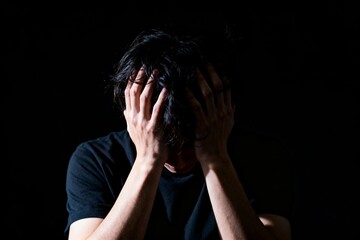 Fototapeta premium Stressed young man holding his head in darkness