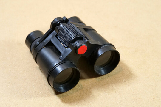 Small black plastic toy binoculars with red center detail on a brown surface, close-up of a children&rsquo;s observation, exploration and pretend play accessory with copy space, no people