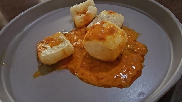 chinese food chicken,Golden cow skin crisps pieces ,Minangese in West Sumatra Indonesia called Kerupuk jangek or Kerupuk kulit rest on a muted plate. Vibrant orange spicy curry sauce pours over them w