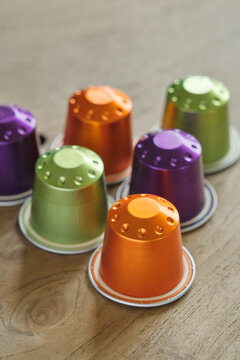 Closeup of colorful coffee capsules in green, orange and purple on a wooden table..	