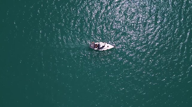 Top down aerial view of sailboat cruising in deep turquoise ocean water
