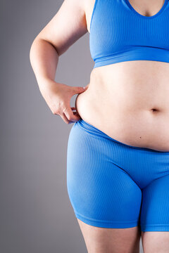 Overweight woman in blue sportswear showing belly fat and cellulite, weight loss and abdominal distention concept