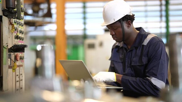 Factory engineer inspecting industrial machine, laptop monitoring, equipment maintenance, production process, manufacturing technology, factory operation, industrial engineering.