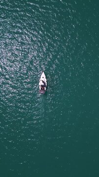 Top down aerial view of sailboat cruising in deep turquoise ocean water