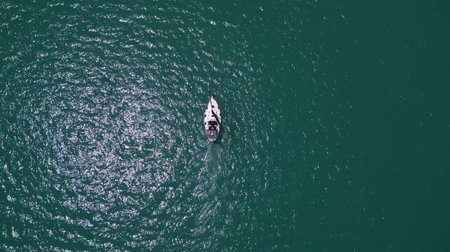 Top down aerial view of sailboat cruising in deep turquoise ocean water
