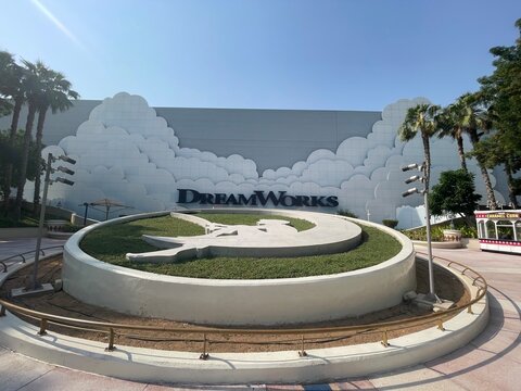 Iconic DreamWorks entrance with the famous boy on the moon logo in a circular planter under a clear blue sky at a modern theme park.