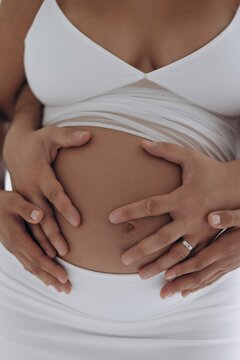 Close-up of pregnant woman belly with husband hands hugging from behind