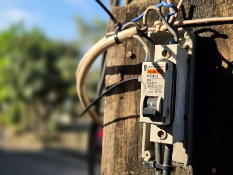 Indonesia - April 26, 2026 : Closeup view of electrical MCB from MERLIN GERIN ELECTRIC brand on pole with blurred background. Industrial photography concept design. Sunlight and shadow at hot day.