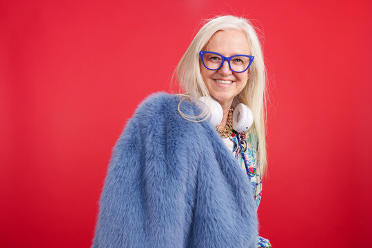 Senior woman smiling, wearing a blue fur coat, headphones, and glasses