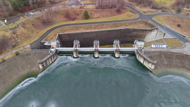 In Świnna Poręba, the Zapora Świnna Poręba dam spans the frozen Mucharskie reservoir beside forests and village areas, shown from a drone perspective in winter.