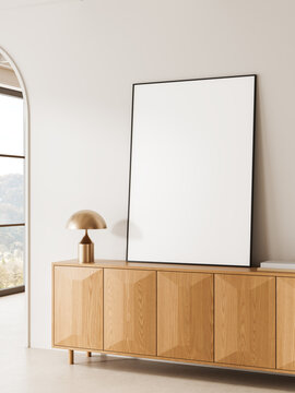 Minimal interior scene with large blank poster leaning on wooden cabinet beside modern lamp in bright room with soft daylight and clean design. 3D Rendering