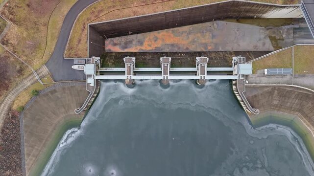 In Świnna Poręba, Poland, the Zapora Świnna Poręba dam spans the frozen surface of Jezioro Mucharskie beside surrounding forests and villages, captured from a drone.