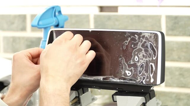 A man wrapping a protective PPF film on a car monitor. The protective glass or film protects the monitor from scratches, fingerprints and other mechanical damage. Wrapping a protective film. 