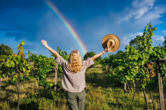 Happy woman farmer enjoying working in vineyard with rainbow on sky after summer rain