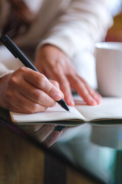 Vertical closeup image of a woman writing on a notebook on the table