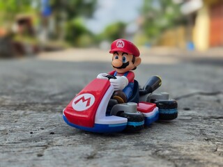 Obraz premium Indonesia - May 10, 2026 : Mini toy of action figure at outdoor with blurred background. Miniature photography concept design. Minifigure of Mario Bros character from Cartoon Gaming with his car.