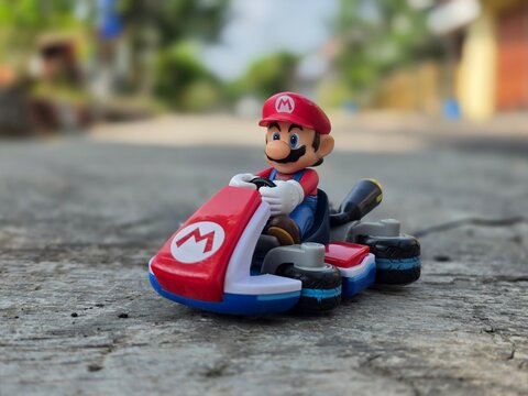 Indonesia - May 10, 2026 : Mini toy of action figure at outdoor with blurred background. Miniature photography concept design. Minifigure of Mario Bros character from Cartoon Gaming with his car.
