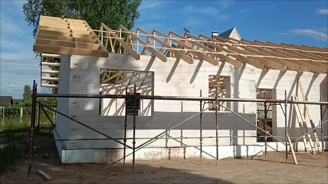 Wooden roof rafters installation and framing process on block walls of a new house construction site with scaffolding.