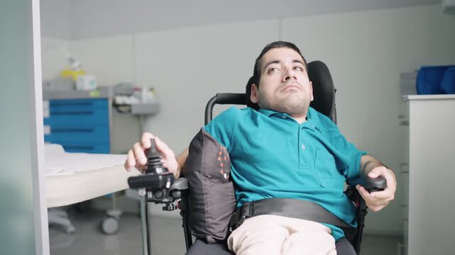 Young disabled man with spina bifida sitting in an electric wheelchair. A therapist assists him during a physical therapy session at a hospital