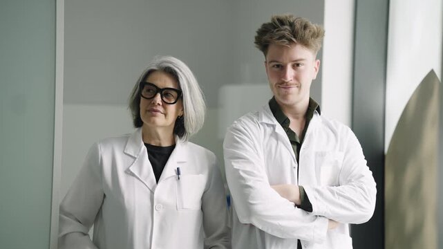Portrait of a senior female scientist and her young male intern looking at the camera. Professional and confident medical research team