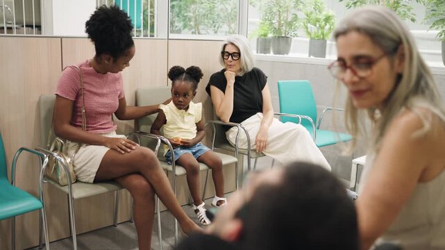 Diverse group of people sitting in a hospital waiting room. A man with spina bifida is in the foreground, talking with a woman