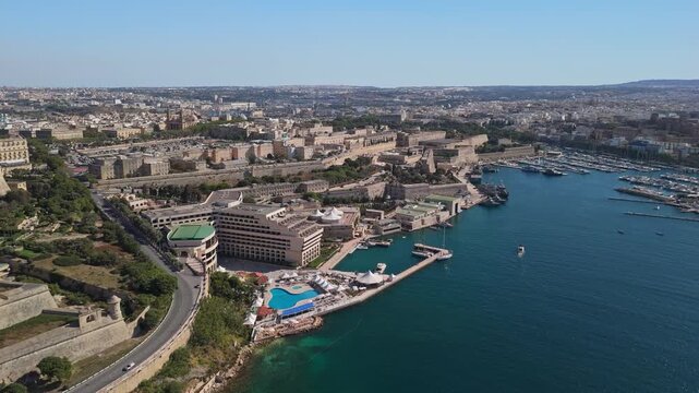 An aerial view over Floriana in Malta captures the urban skyline along Marsamxett Harbour with its waterfront marinas, boats, and historic fortifications set beside clear Mediterranean waters.