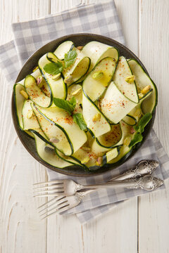 Zucchini carpaccio with pistachios, chili pepper and mint close-up in a plate on the table. Vertical top view from above